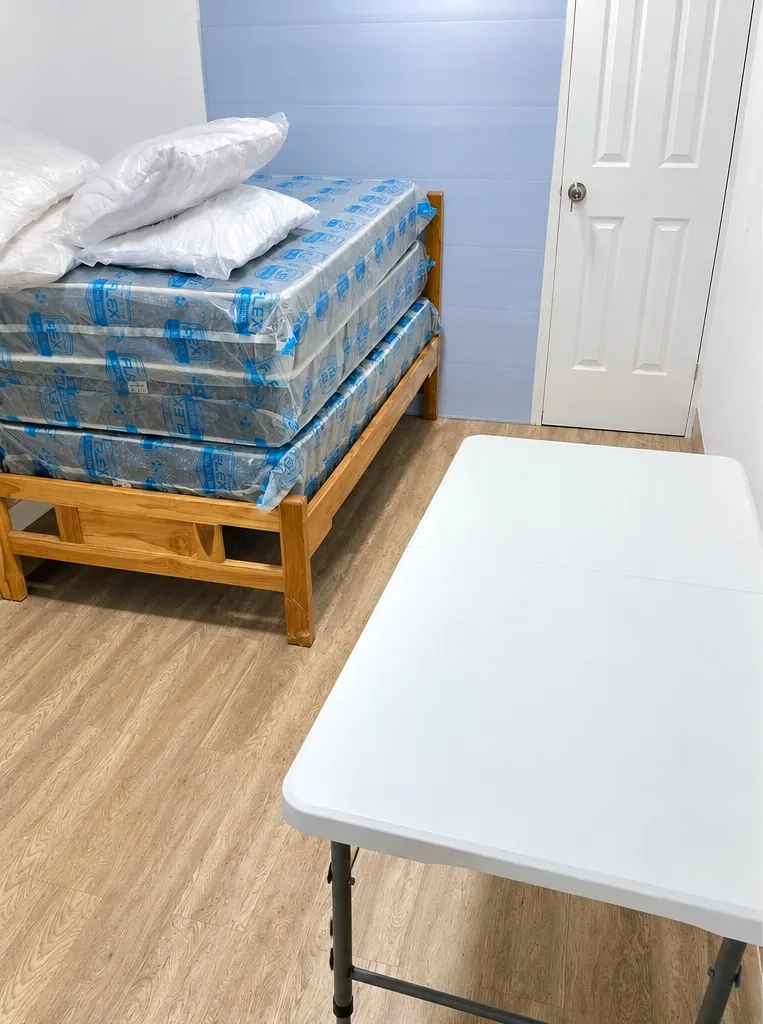 Interior del contenedor de vivienda con cama, colchones nuevos, almohadas y mesa